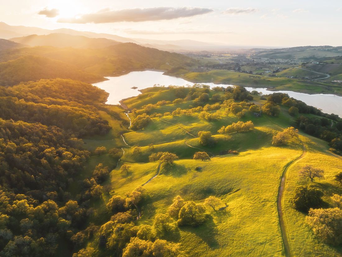 Rolling oak-studded ranch land beside a reservoir at sunset